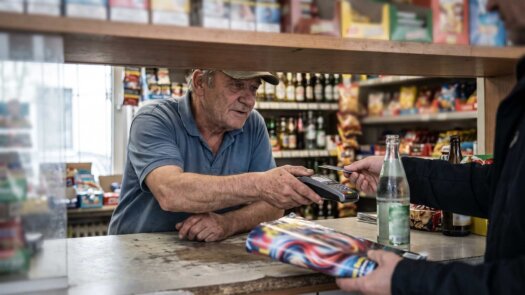 Kioskbesitzer reicht einem Kunden das Kartenterminal über den Tresen