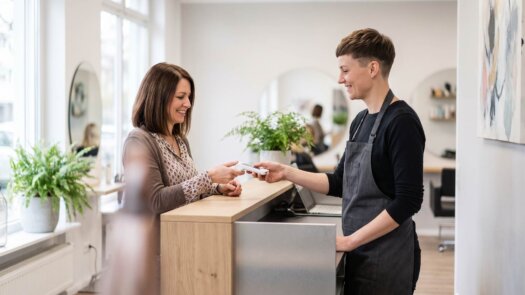 Friseurin reicht ihrer Kundin an der Rezeption den Kartenleser