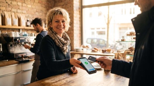 Caféinhaberin reicht einem Kunden das Kartenterminal über den Tresen